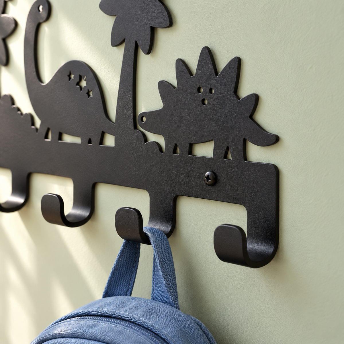 Detail van de zwarte structuurpoedercoating, dinosaurus-uitsparingen en gebogen haken van de metalen kinderkapstok.