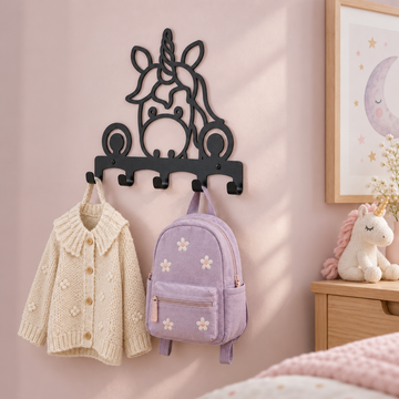 Zwarte metalen eenhoornkapstok aan een zachtroze muur, met een crème vest en lila kinderrugzak.