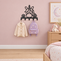 Zwarte eenhoornkapstok van verder weg in een kinderkamer met een roze muur, houten kast en eenhoornknuffel.