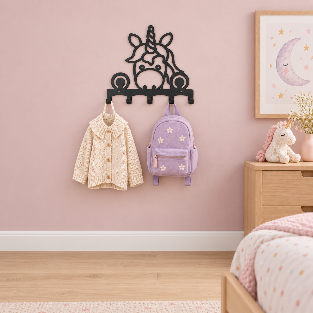 Zwarte eenhoornkapstok van verder weg in een kinderkamer met een roze muur, houten kast en eenhoornknuffel.