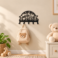 Zwarte stalen kinderkapstok met boerderijdieren en vijf haken, met een beige rugzakje aan de muur in een warme kinderkamer.