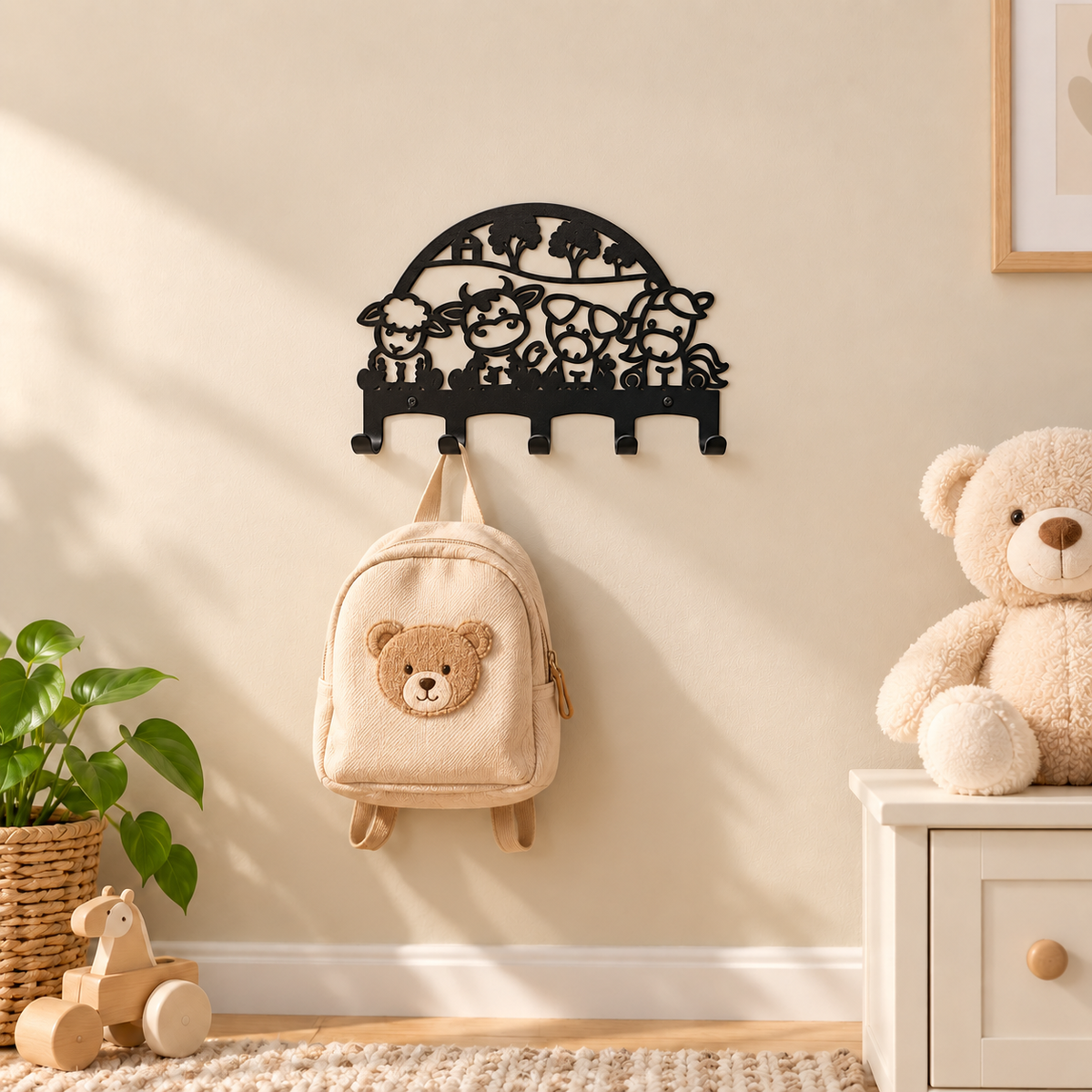 Zwarte stalen kinderkapstok met boerderijdieren en vijf haken, met een beige rugzakje aan de muur in een warme kinderkamer.
